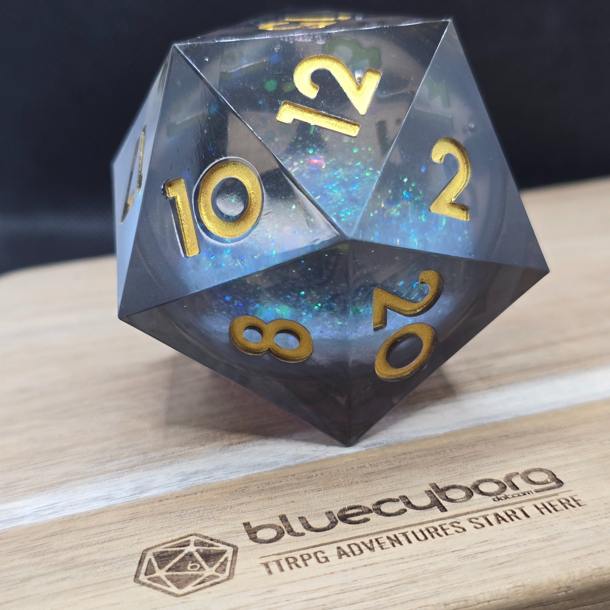 Stormglass Chonk 55mm liquid core D20 with smoky clear resin, blue shimmer core and gold numbers